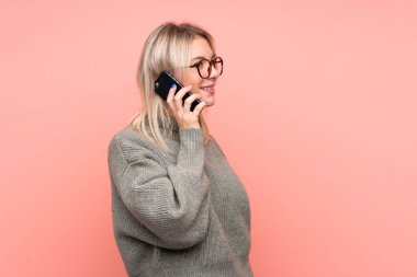 Soyutlanmış pembe arka planı olan genç, sarışın bir Rus kadın cep telefonuyla sohbet ediyor.