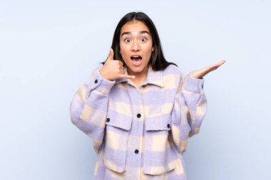 Genç Hintli bir kadın mavi arka planda izole edilmiş telefon hareketlerinde ve şüphelerinde