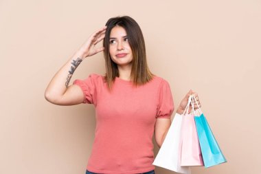 Alışveriş çantasıyla izole edilmiş arka planda kuşkuları olan ve kafası karışmış genç bir kadın.