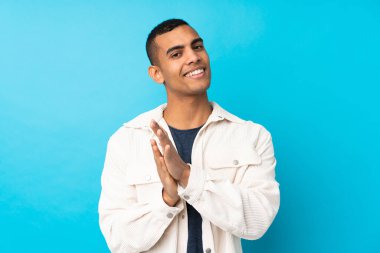 Genç Afro-Amerikalı bir adam mavi arka planda bir konferansta sunumdan sonra alkışlıyor.