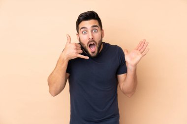 Beyaz tenli yakışıklı adam bej arka planda izole edilmiş telefon jestleri yapıyor ve şüpheli.