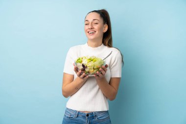 Genç esmer kadın mavi arka planda salata tutuyor.