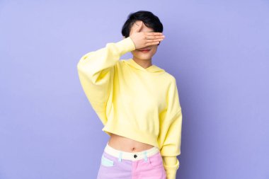 Genç Vietnamlı bir kadın, kısa saçlı, tek başına mor arka planda, gözleri elleriyle kapatıyor. Bir şey görmek istemiyorum.