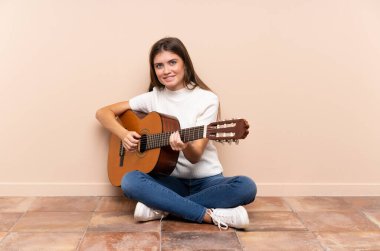 Gitarlı genç kadın yerde oturuyor.