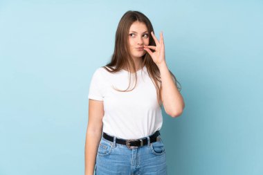 Mavi arka planda izole edilmiş genç beyaz kız sessizlik işareti gösteriyor.