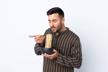 Arka planda izole edilmiş genç bir adam elinde çubuklu bir kase erişteyle sıcak oldukları için onu üflüyor.