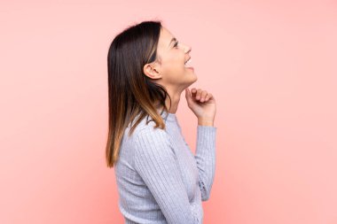 Soyutlanmış pembe arka plandaki kadın yan yana gülüyor.