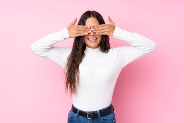 İzole edilmiş pembe arka planı olan genç bir kadın elleriyle gözlerini kapatıyor.