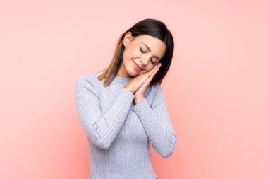 Soyutlanmış pembe arka planda bir kadın uyku jesti yapıyor.