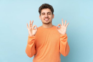 Beyaz adam Zen pozunda mavi arka planda izole edilmiş.