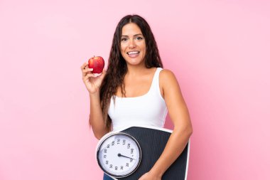 Soyutlanmış pembe arka plan, tartı makinesi ve elması olan genç bir kadın.