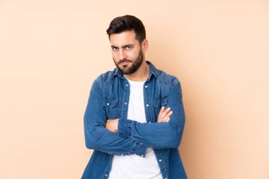 Beyaz tenli yakışıklı adam bej arka planda izole edilmiş ve mutsuz bir ifadeyle.