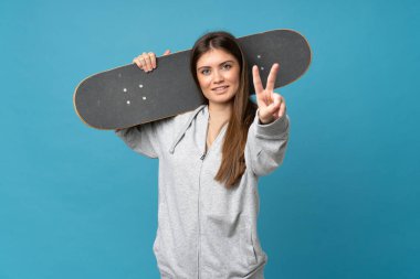 Genç bir kadın mavi arka planda paten kayıyor ve zafer jestleri yapıyor.