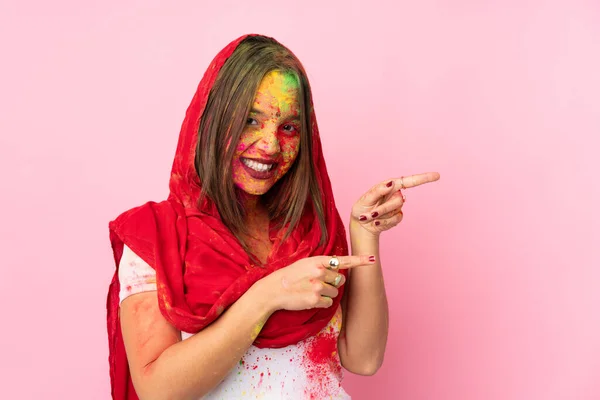 年轻的印度妇女 满脸五颜六色的全麦粉 被粉色背景隔离 手指指向侧面 并展示了一种产品 — 图库照片