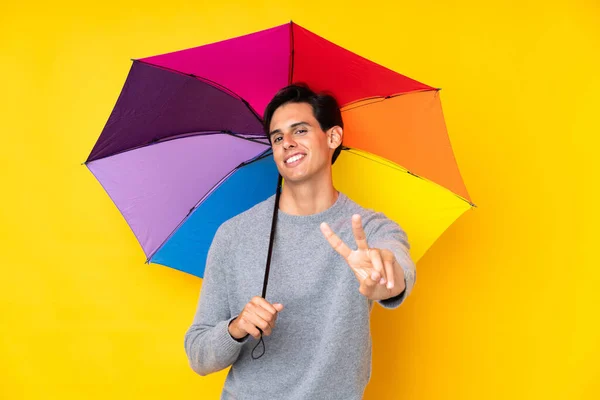 Muž Drží Deštník Nad Izolovaným Žlutým Pozadím Usmívá Ukazuje Znamení — Stock fotografie