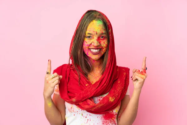 Young Indian woman with colorful holi powders on her face isolated on pink background pointing up a great idea