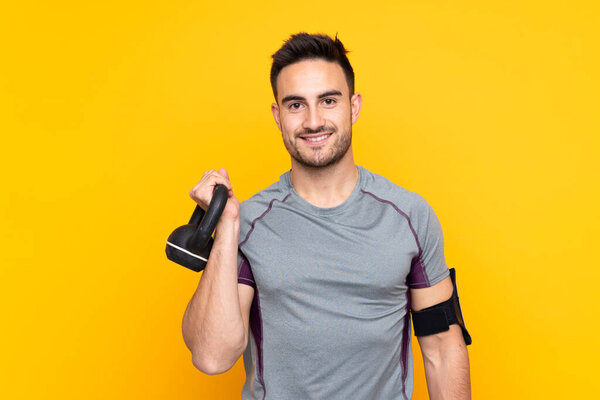 Sport man over isolated yellow wall making weightlifting with kettlebell