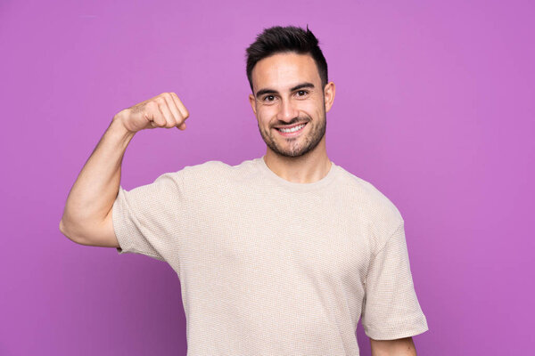 Young handsome man over isolated purple background doing strong gesture