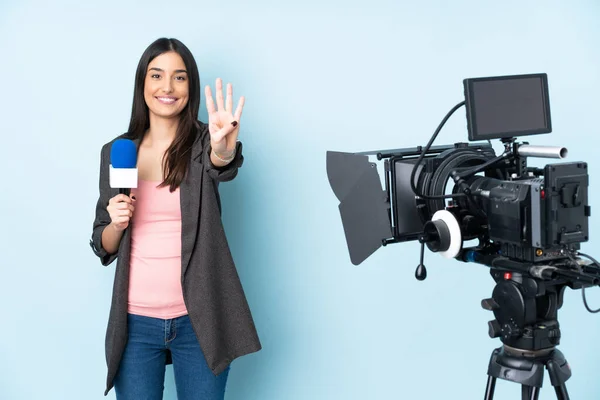 Reporter woman holding a microphone and reporting news isolated on blue background happy and counting four with fingers