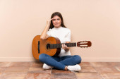 Mladá žena s kytarou sedící na podlaze nešťastná a něčím frustrovaná. Negativní výraz obličeje