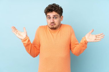 Beyaz adam mavi arka planda izole edilmiş, şüphe uyandıran hareketler yapıyor.