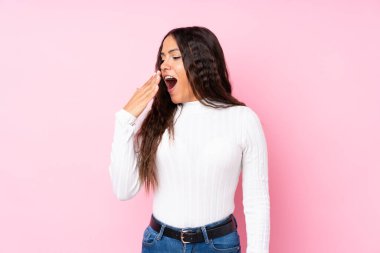 Soyutlanmış pembe arka planda genç bir kadın esniyor ve elleriyle ağzını kapatıyor.