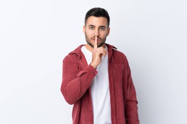 Sakallı, kadife ceket giyen, izole edilmiş beyaz arka planda sessiz bir jest işareti gösteren genç ve yakışıklı bir adam. Parmağını ağzına sok.