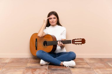 Gitarlı genç bir kadın yerde mutsuz ve hayal kırıklığına uğramış bir şekilde oturuyor. Olumsuz yüz ifadesi