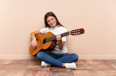Gitarlı genç kadın yerde oturuyor.