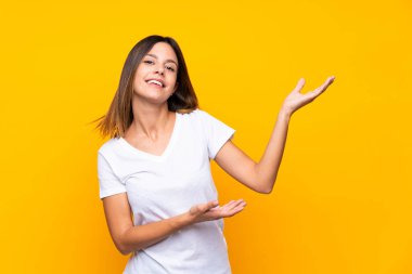 Izole sarı arka plan üzerinde genç kadın gelmeye davet için yan ellerini uzatarak