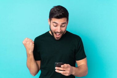 Beyaz tenli yakışıklı adam mavi arka planda izole edilmiş, şaşırmış ve bir mesaj gönderiyor.