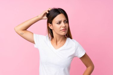 Soyutlanmış pembe arka planı olan genç bir kadın kafasını kaşırken şüpheye düşüyor.