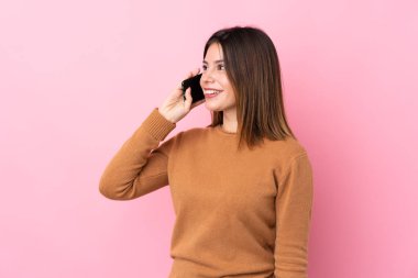 İzole edilmiş pembe arka planı olan genç bir kadın cep telefonuyla sohbet ediyor.