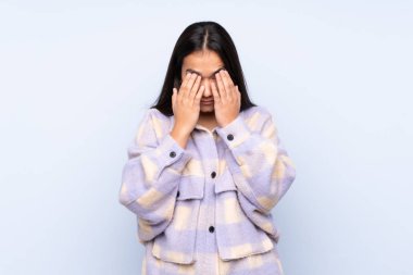 Genç Hintli kadın mavi arka planda izole edilmiş, yorgun ve hasta bir ifadeyle