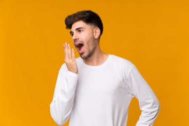 Genç adam izole edilmiş turuncu arka planda esniyor ve elleriyle ağzını kapatıyor.