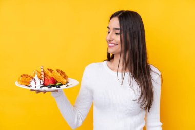 Genç esmer kadın, izole edilmiş arka planda mutlu bir ifadeyle waffle tutuyor.