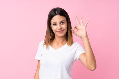 İzole edilmiş pembe arka planda genç bir kadın parmaklarıyla işaret veriyor.