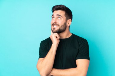 Beyaz tenli yakışıklı adam mavi arka planda izole edilmiş, yukarı bakarken bir fikir düşünüyor.