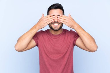 Sakallı, genç, yakışıklı, soyutlanmış, mavi arka planda, gözleri elle kaplanmış.