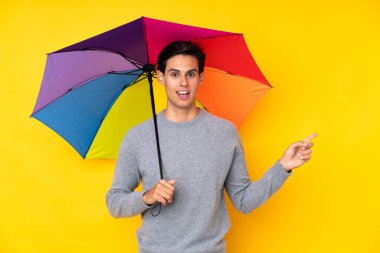 Sarı arka planda şemsiye tutan adam şaşırdı ve parmağını yana çevirdi.