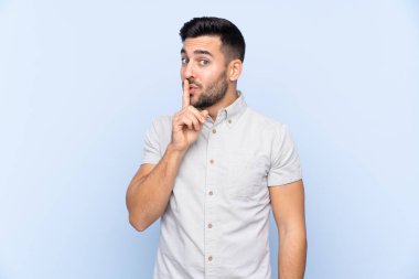 Sakallı, mavi arka planda genç ve yakışıklı bir adam sessizlik hareketi yapıyor.