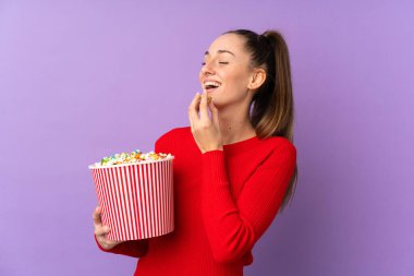 Genç esmer kadın, izole edilmiş mor arka planda elinde koca bir kova patlamış mısır tutuyor.