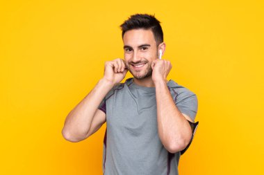 İzole edilmiş sarı duvardaki spor adamı müzik dinliyor.