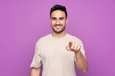 Genç, yakışıklı, soyutlanmış, mor arkaplan, şaşırmış ve ön tarafı işaret ediyor.