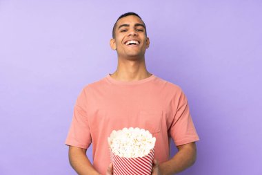 Genç Afrikalı Amerikalı bir adam mavi arka planda elinde koca bir kova patlamış mısır tutuyor.