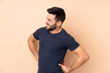 Beyaz tenli yakışıklı adam, bej arka planda izole edilmiş. Çabaladığı için sırt ağrısı çekiyor.