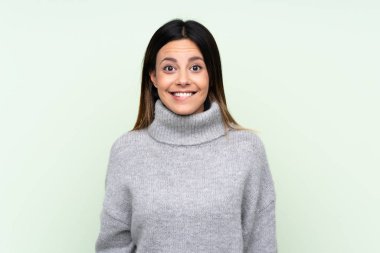 Yeşil arka planda kazak giyen kadının şüpheleri ve kafası karışmış yüz ifadesi var.