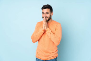 Beyaz tenli yakışıklı adam avucunu bir arada tutuyor. Kişi, izole edilmiş mavi bir arkaplan istiyor.