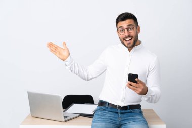 Genç işadamı cep telefonunu tutuyor ve davet etmek için elini yana açıyor.