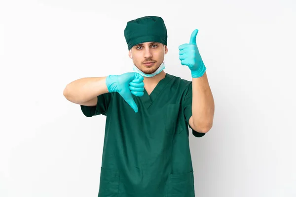 Surgeon in green uniform isolated on isolated white background making good-bad sign. Undecided between yes or not